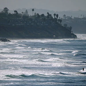 People enjoy the beach and waves on an autumn day along the coast in Carlsbad California